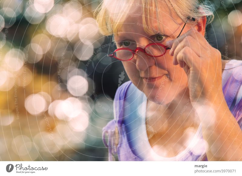 AST10 l A sympathetic woman looks over her glasses, holds them tightly and smiles slightly. She is framed with many lens lights Woman Smiling kind