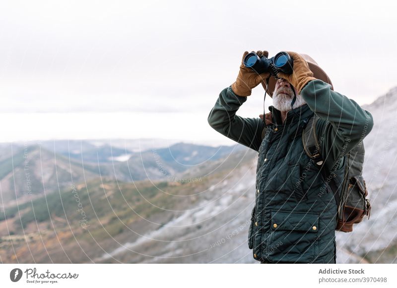 Elderly man looking through binoculars in mountains traveler observe admire highland winter senior outerwear male caceres extremadura spain picturesque terrain