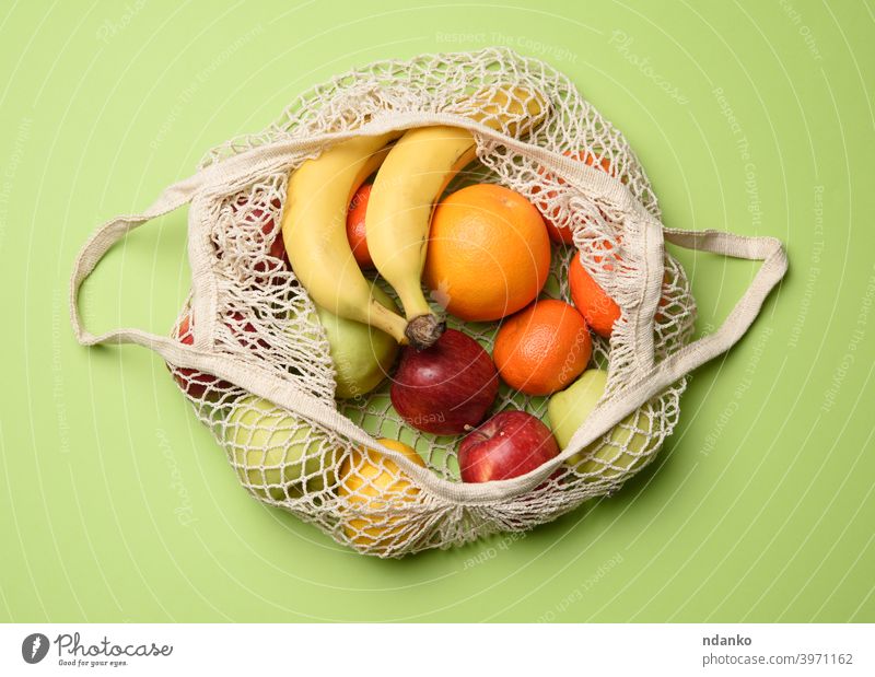 ripe fresh fruits in a textile string bag on a green background, top view mesh healthy natural reusable organic food vegetarian market shopping vegan eco