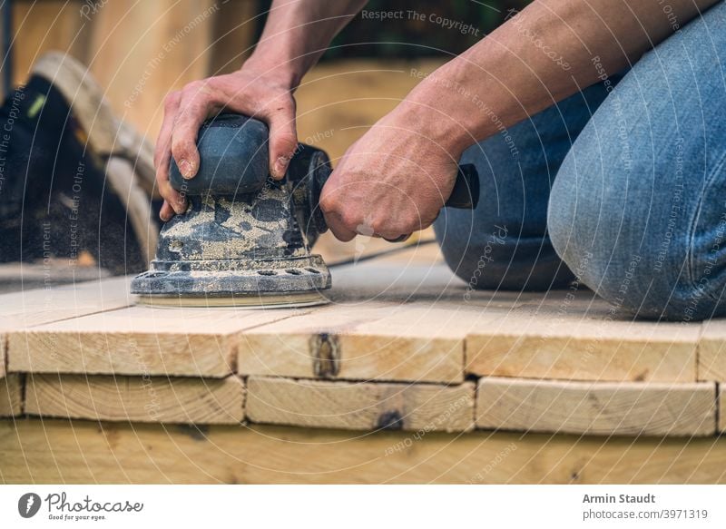 close up of a worker sanding wood planks with a grinder machine knees hand arm working closeup dust grinding tool equipment carpenter craft construction sander