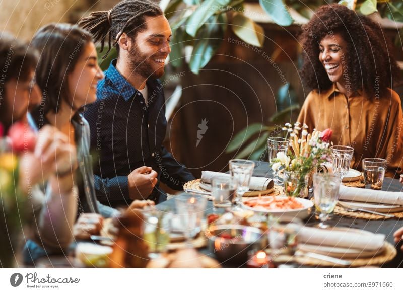 happy group of friends sitting at table having dinner together Adult Candid Outdoor Young Adult alcohol backyard celebrating chatting dinner party diversity