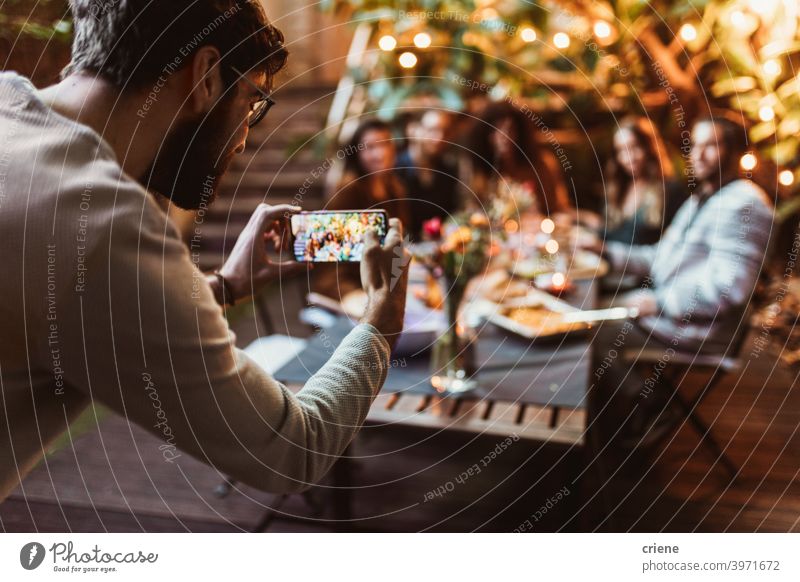 young adult taking photo of his friends with phone at dinner party Adult Candid Outdoor Smartphone Young Adult alcohol backyard celebrating chatting diversity