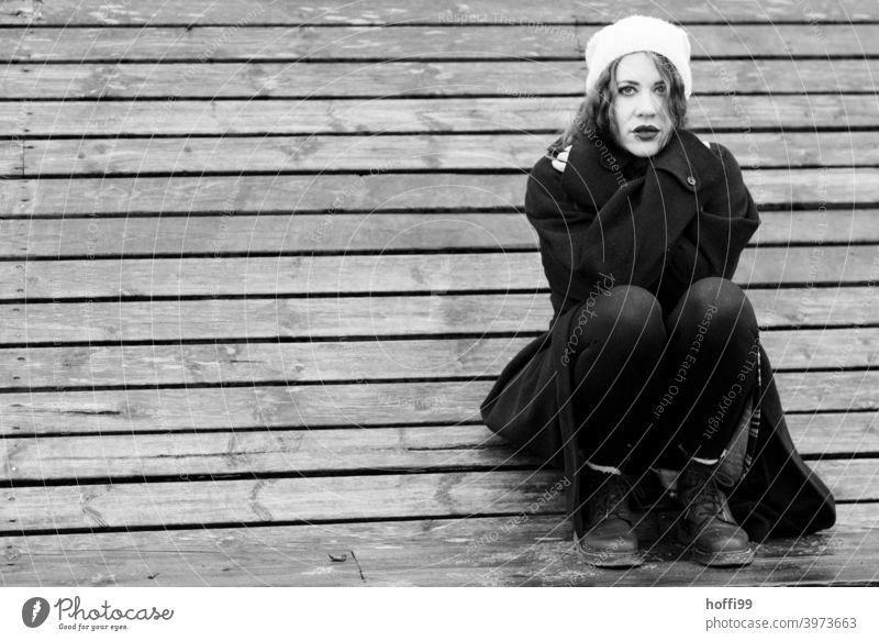 the young woman squats on a bench and looks into the camera Woman crossed arms Coat Looking into the camera long coat portrait Lifestyle Authentic pretty