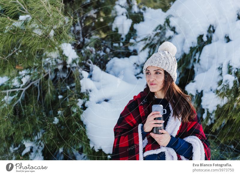 beautiful woman wrapped in plaid blanket holding thermos with hot drink. nature and lifestyle hot tea mountain sunny snow hiking winter cold covered caucasian