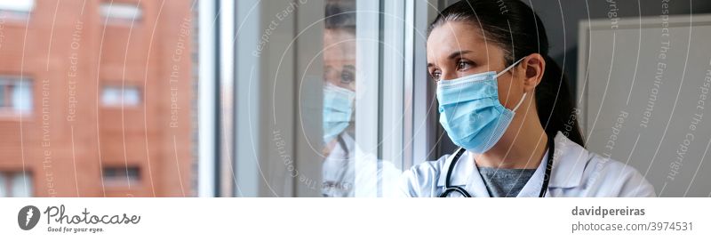 Female doctor looking out the hospital window female protective mask thoughtful reflection serious coronavirus banner web header panorama panoramic copy space