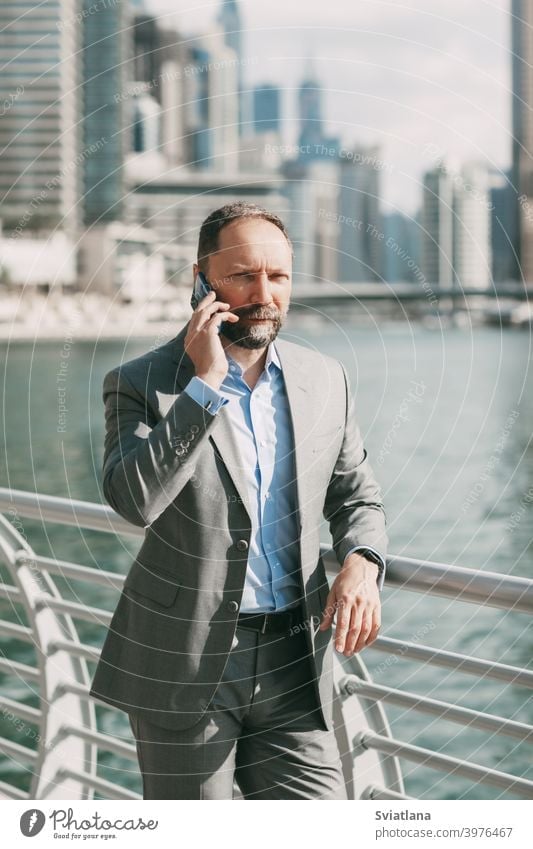 Young businessman with a phone in his hands, standing in a big city among high-rise buildings office smartphone modern successful suit happy employer flash
