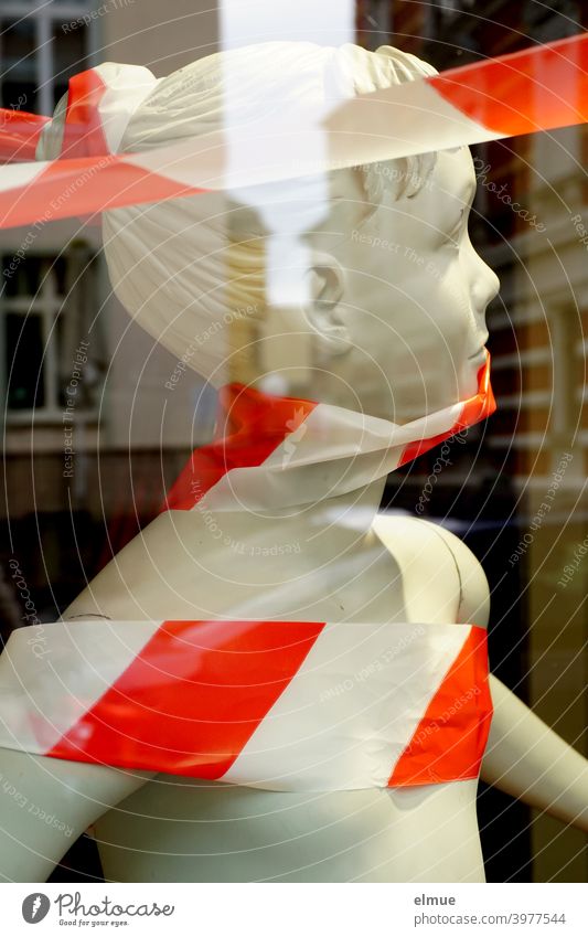 In the shop window is a white, childlike mannequin with red and white barrier tape wrapped around it / business liquidation / clearance sale / sale Mannequin