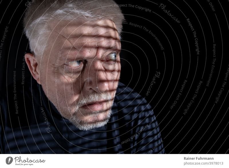 A man sits in the darkness. He looks through a grate into a bright light. Light Shadow Man portrait Grating Lonely on one's own Loneliness Sadness sad