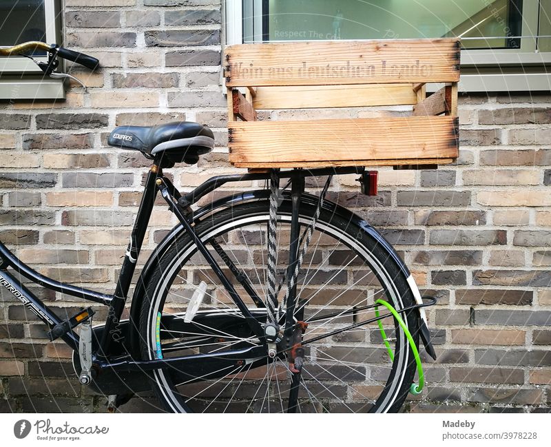 Black Dutch bike with rustic wooden box on the luggage rack and green lock in front of old brown brick wall at the harbour of Münster in Westphalia in the Münsterland region of Germany