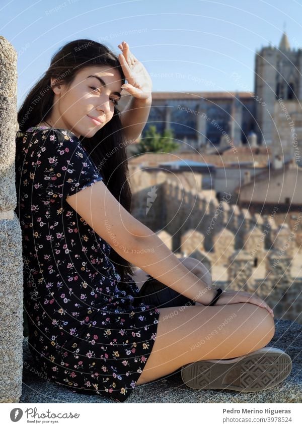 Beauty woman covering the sun with her hand, sitting on a wall women beauty white girl caucasian brown hair model dress cathedral avila spain sunny clear sky