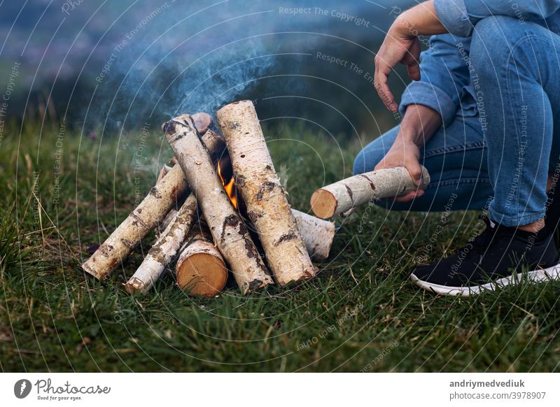 traveler man on camping in the mountains outdoor. setting up camping fire. forest winter match young flame firewood nature bonfire tourism campfire male pile