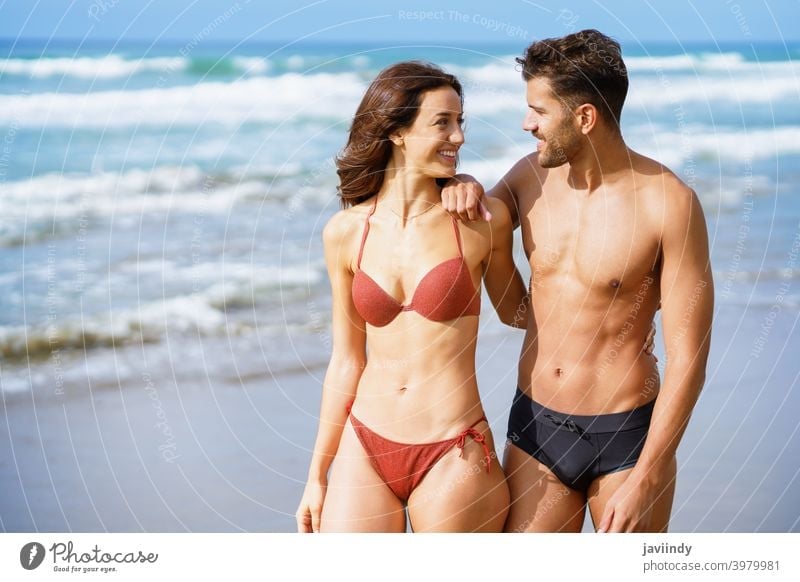 Young couple of beautiful athletic bodies walking together on the beach woman bikini summer body leisure lifestyle female girl coast outdoors enjoying people