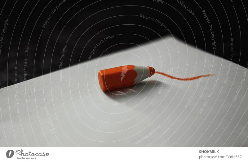 an orange button in form of a pencil lying on white paper and making an orange line on it color colour Abstract Drawing object Object photography