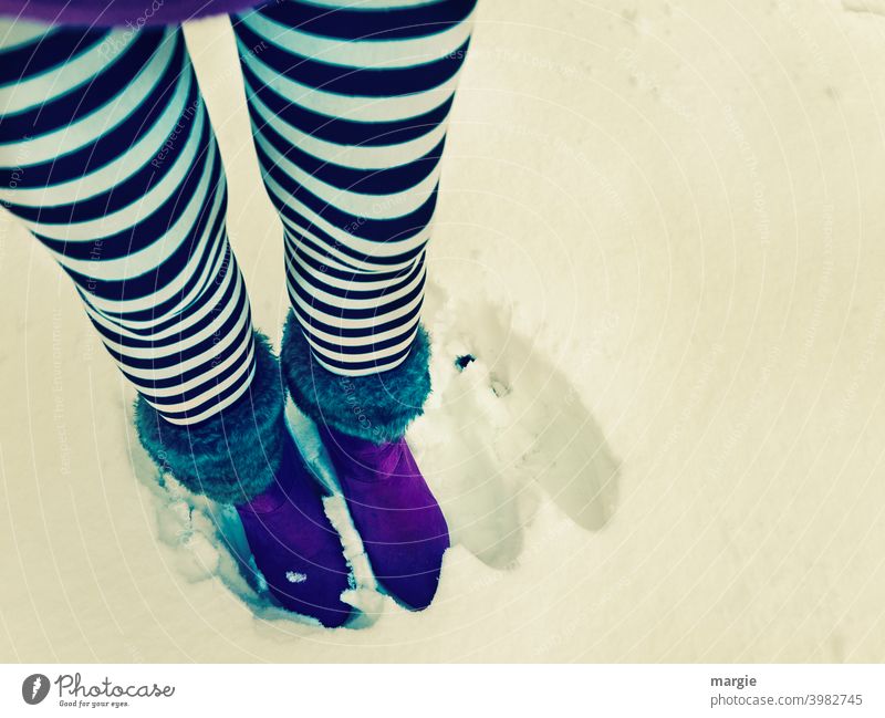 A woman is standing in the snow.  Next to her two empty footprints. She wears black and white striped stockings and purple boots. Footwear Boots Snow Feet Legs