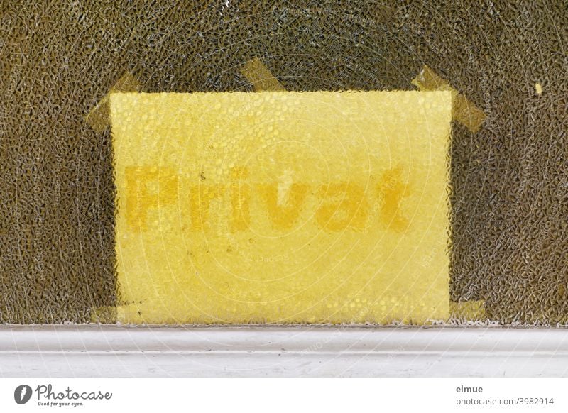 Behind the textured glass pane of a door, a light yellow note with yellow writing "Private" was attached by means of several adhesive strips / Privacy