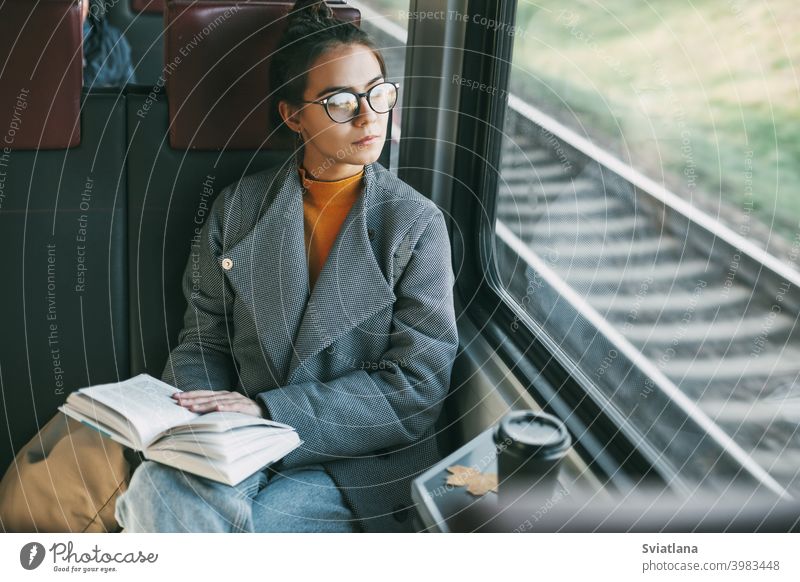 Young beautiful girl on a train reading a book while traveling in a train passenger happy journey coffee tourist calmness inside transport young sitting trip