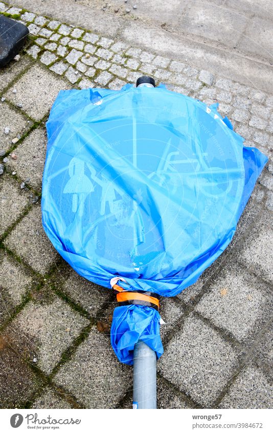 A traffic sign (traffic sign no. 241-31) covered with a blue transparent garbage bag is lying on grey cobblestone pavement Road sign footpath and cycleway