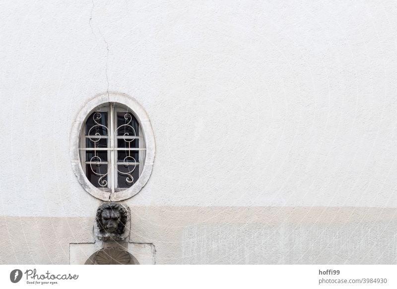 a barred oval window with a lion head on a grey wall Oval latticed Round barred windows old town house Gray round window Window Exceptional Minimalistic