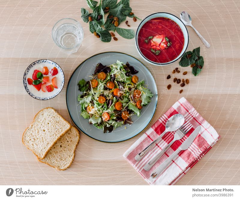 Bird's eye of a healthy meal. Lettuce salad with cherry tomatoes, two pieces of bread, yogurt with strawberries and a typical Russian soup called Borscht.