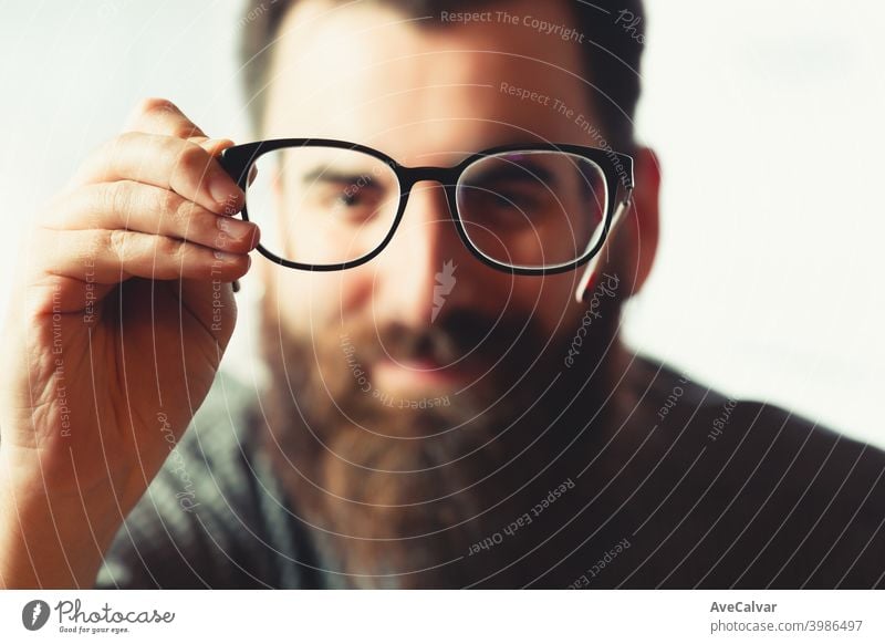 An out of focus hipster male holding a pair of blue light glasses on focus to camera while smiling 20s contemplation entrepreneur genius technology headshot