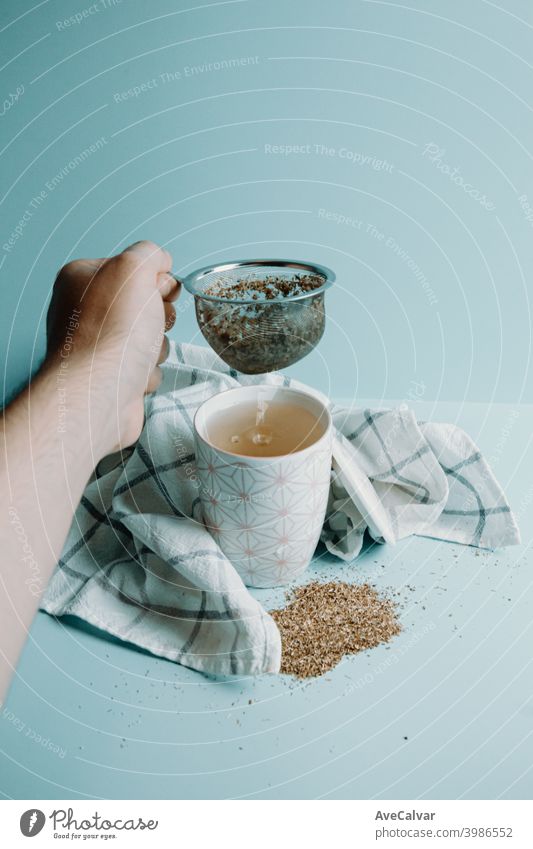 A hand grabbing a tea distiller over a cup of tea over a pastel blue background colours conceptual healing horizontal relaxing simplicity office fun relaxation