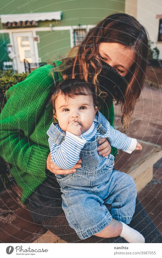 Image in green tones of a young single mom with her baby during covid pandemic coronavirus mother family motherhood mask face mask risk contagious influenza