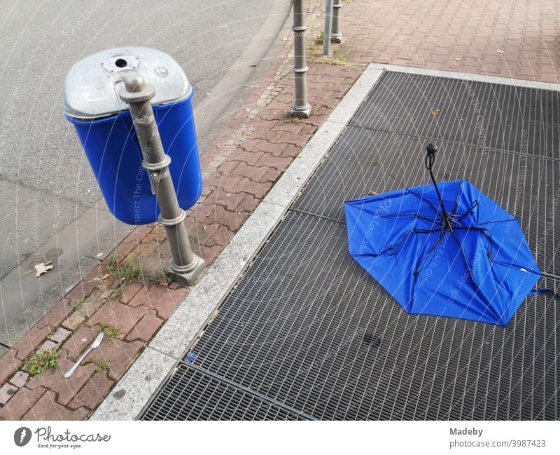 Blue garbage home next to and blue umbrella on the ventilation grille of a subway station at the Senckenberganlage in the Westend of Frankfurt am Main in Hesse, Germany