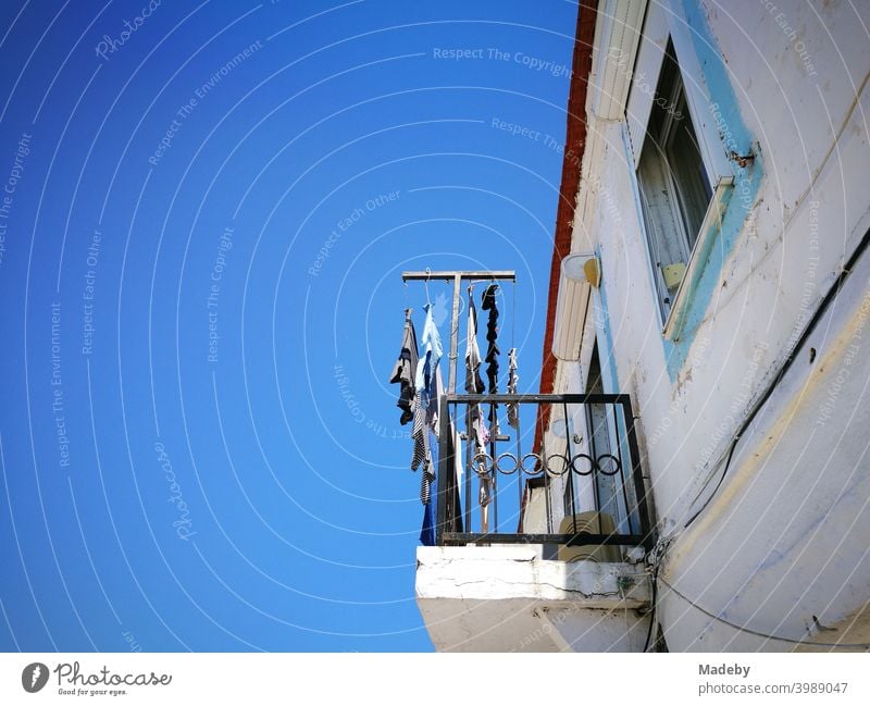 Old white house with balcony and clothesline in front of a bright blue sky in summer sunshine in Alacati near Izmir at the Aegean Sea in Turkey Balcony rail