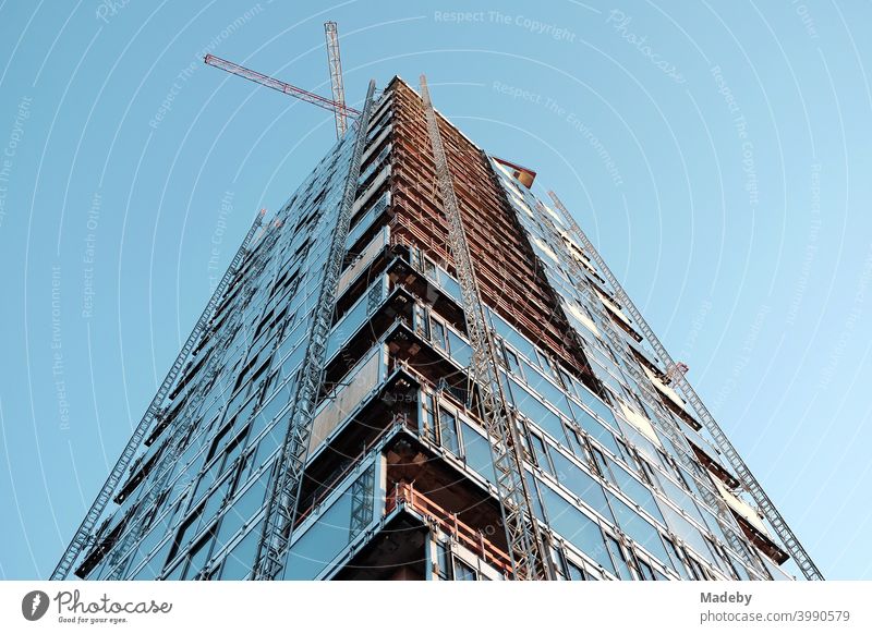 Shell of a modern high-rise building with luxury apartment with two construction cranes in front of a light blue sky in the West End of Frankfurt am Main in Hesse, Germany