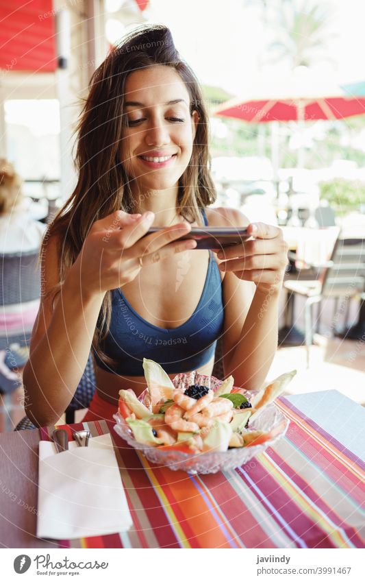 Young woman photographing her salad with a smartphone while sitting in a restaurant food healthy mobile table lunch young photography camera lifestyle female