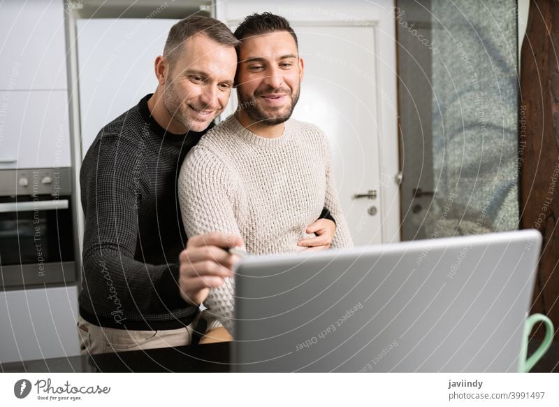 Romantic Gay couple working together at home with their laptops. gay men teleworking hug homosexual hugging lgbt lgbtq male relationship boyfriend people 30s