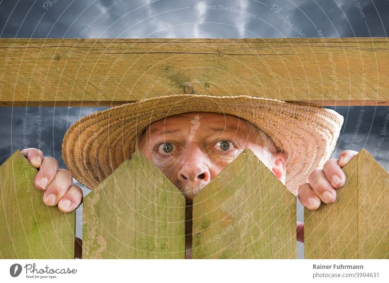 A curious man peers over a garden fence. He is wearing a straw hat. Thunderclouds can be seen in the background. Man Neighbor Curiosity inquisitorial Spy