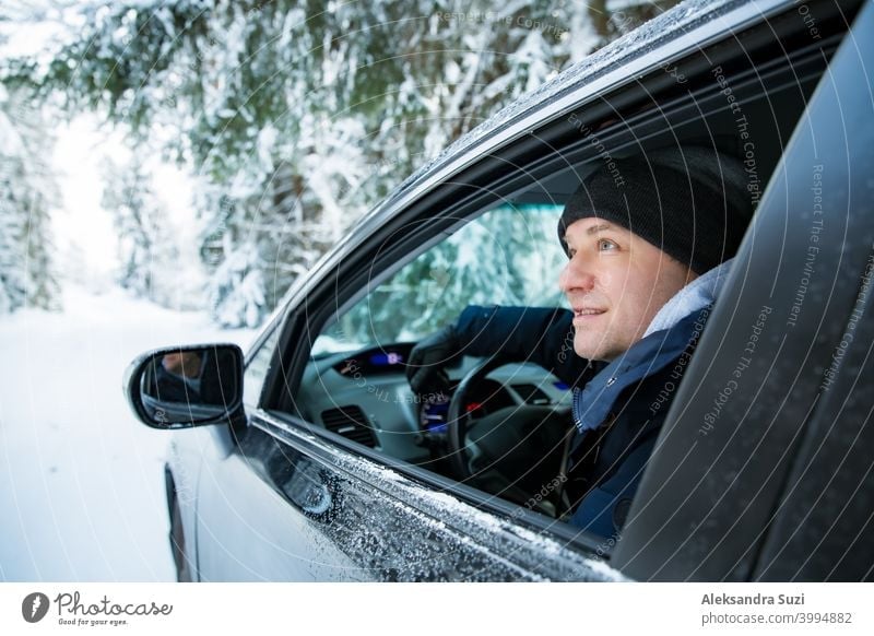 Man in warm winter clothes sitting in car. Snowy winter country road, car covered with ice, Beautiful forest under the snow. auto blizzard cold commute