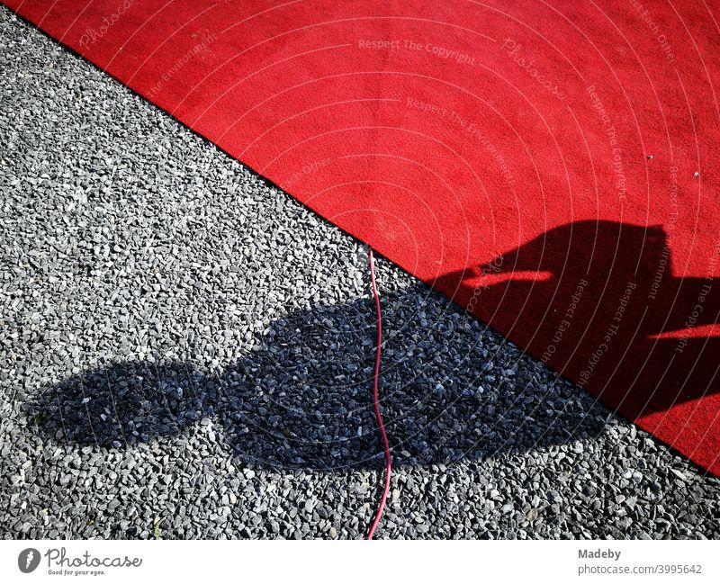 Shadow of a woman with a handbag on a red carpet and grey pebbles at a vernissage in Oelde near Warendorf in Westphalia, Germany Red carpet Vernissage
