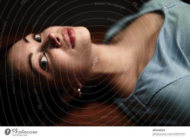 Portrait of a young beautiful brunette woman lying on a wooden table in a dark room and looking upwards Young woman pretty Brunette Long-haired Slim teenager