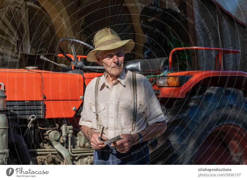 Old farmer working on red tractor under roof of farmhouse in sunshine. more adult aged Agriculture car automobile Car Caucasian Characters test Landscape