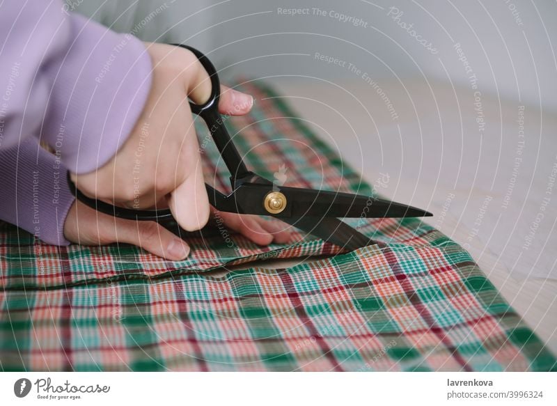 Tailor hand hold scissors cut fabric material for sewing. Closeup of work  process of clothes creation in workshop studio or professional atelier.  Garment industry and dressmaking occupation concept Stock Photo