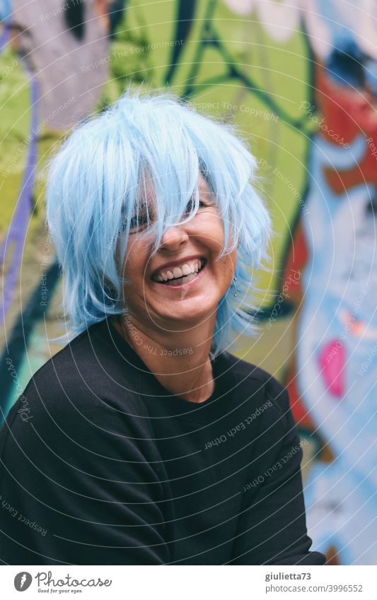 Portrait of a happy, laughing woman / artist with blue hair Looking into the camera Front view Upper body portrait Central perspective Shallow depth of field