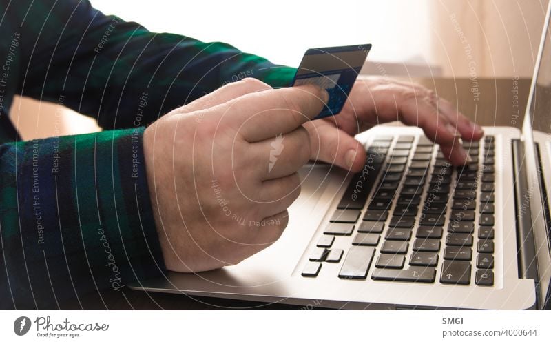 Close-up of a a hand holding a credit card in front of a laptop. Concept of card payment on the internet. adult banking bill buying checkout commerce computer
