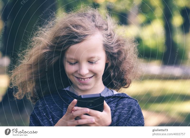 Portrait of happy boy with long hair reading funny messages on his mobile phone Front view Upper body portrait Central perspective Downward