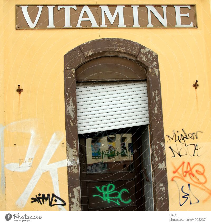 crooked and crooked - dilapidated entrance door with crooked blinds in yellow wall with graffiti and the writing VITAMINE above the door Wall (building) Facade
