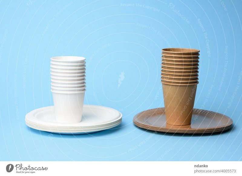 stack of white and brown paper cups and round plates on a blue background craft cutlery dining dinnerware dish disposable drink eco ecological empty
