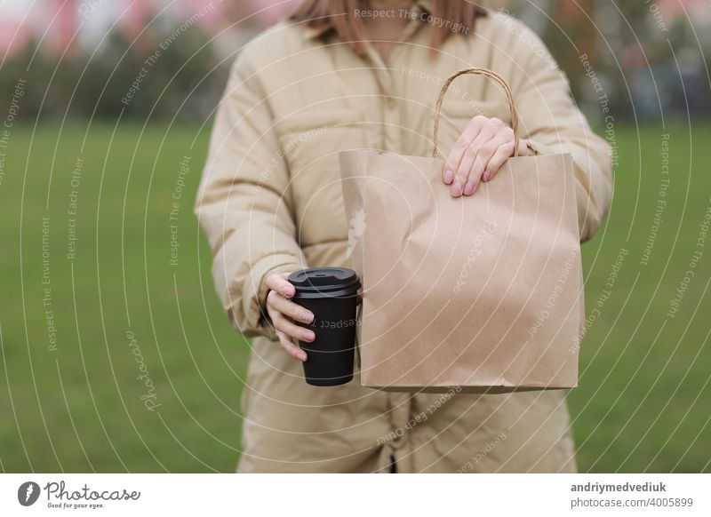 Takeaway cup with coffee, mock up for identity branding. Close-up of paper bag and paper cup in female hand.Young woman carries shopping bags and coffee.