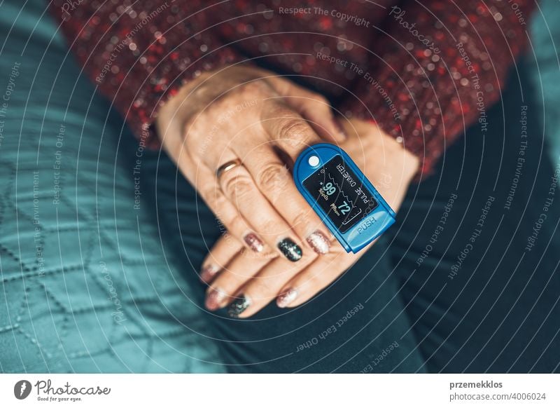Woman measuring the degree of oxygen saturation of the blood and heart rate at home using pulse oximeter. Home treatment of virus. Checking health condition