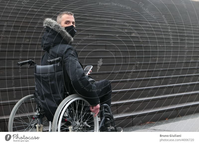 Concept of disabled person. Man in a wheelchair outside in the street in front of staircase. People with smartphone. surgical mask man accessibility disability