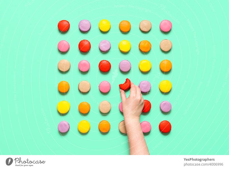 Macarons symmetric aligned on a colored background. Woman hand taking a macaroon, top view above view almond cookies artisanal assortment bakery bite
