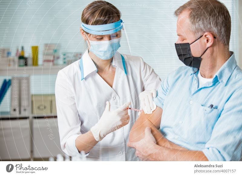 Female doctor with surgical mask and in gloves giving vaccine injection to man in hospital. Vaccination during COVID-19 pandemic arm care clinic coronavirus