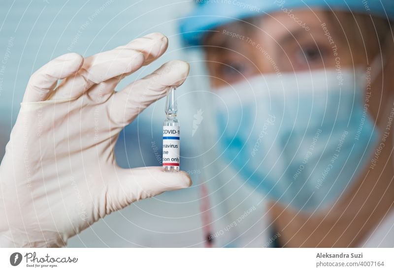 Female doctor with surgical mask and in gloves holding vaccine ampoule and syringe. Vaccination during COVID-19 pandemic arm care clinic coronavirus covid-19