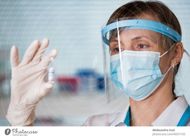 Female doctor with surgical mask and in gloves holding vaccine ampoule and syringe. Vaccination during COVID-19 pandemic arm care clinic coronavirus covid-19