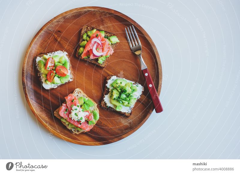 tasty diet food for breakfast or brunch - avocado and salmon toast with cream cheese, cucumber and red onion served on wooden plate sandwich bread snack meal